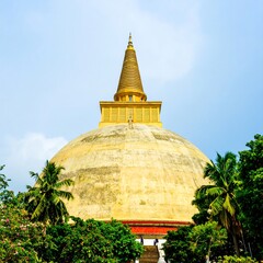 Golden Stupa Temple Surrounded by Lush Greenery and Palm Trees.
