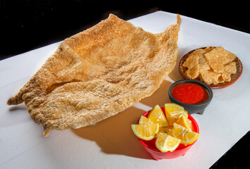 Pork cracklings with spicy red sauce and limes as part of a Mexican snack on a white table....