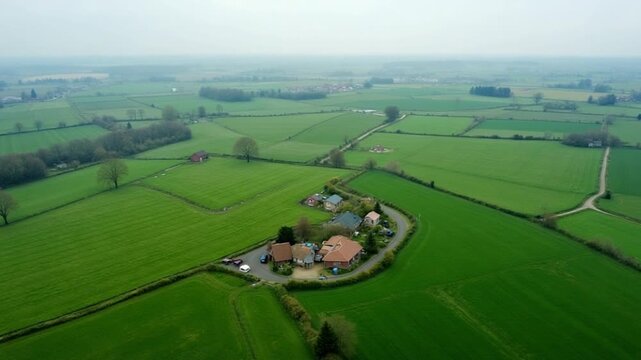 Aerial view of a tranquil rural landscape with scattered houses, lush green fields, and an overcast sky, ideal for themes of agriculture and countryside living