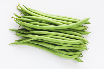 Closeup pile of fresh, raw green beans on a white background, highlighting their long, slender shape and vibrant green color.