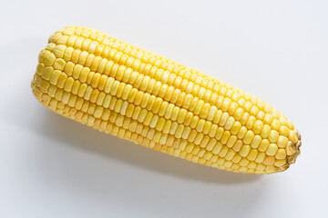 A closeup shot of a single, raw corn cob, showcasing the neat rows of yellow kernels on a white background.