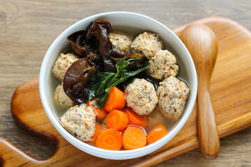 Bakso Lohua soup with meatballs and vegetables in a white bowl. Served on a wooden board for a rustic, home-cooked feel.