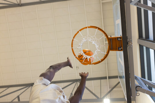 African american man jumping upward toward hoop with white net in gym dunking basketball