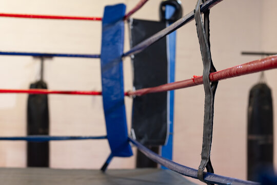 Boxing ring corner post showing interwoven red and blue ropes in gym interior with punching bags