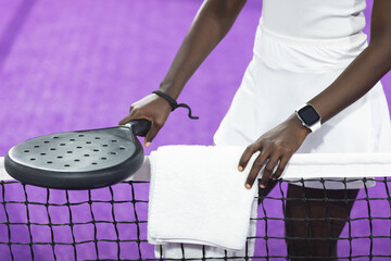 African american woman standing at net on purple padel court with racket and towel