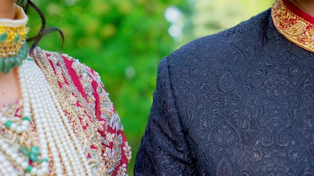 Bride putting a hand on the groom shoulder. Traditional henna painted bridal hand. Red and black colors in the Indian embroidered clothes, Elements of Asian wedding. 