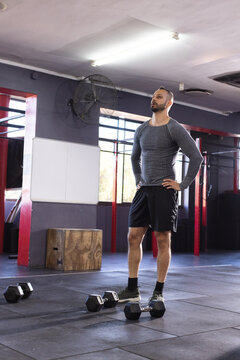 Indian asian man standing wearing athletic top, shorts in gym with hex dumbbells, pull-up rig