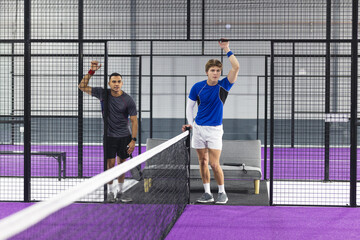 Diverse male athletes standing at padel net in wristbands beside mesh fence, bench