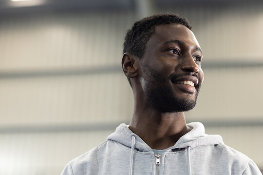 Mid adult african american man standing in warehouse in grey zip-up hoodie smiling, copy space