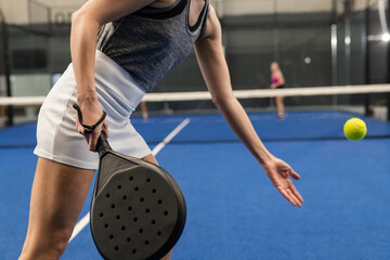 Female opponents in sportswear swinging black racket hitting ball on padel court
