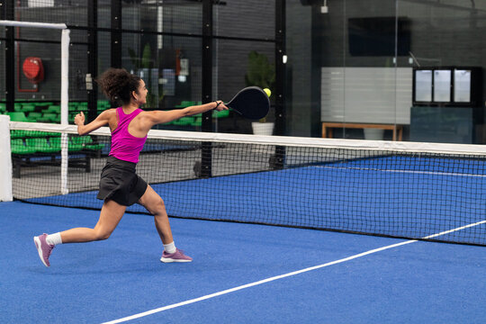 Padel athlete lunging on blue court gripping racket intercepting yellow-green ball above white net