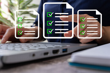 Person in front of a laptop pointing at a document with a check mark list, there are more around