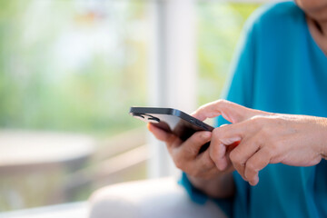Close up senior woman using on smartphone sitting on sofa in living room at home, digital lifestyle, closeup elder asian using smart phone with social media for relax, chatbot or AI.