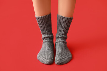 Legs of young woman in warm grey knitted socks on red background