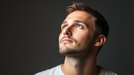 Handsome man with beard looking up thoughtfully against a dark background in a studio setting for inspiration