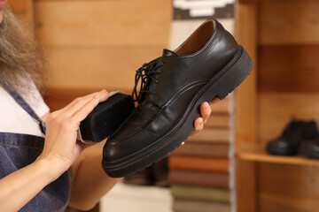 Female shoemaker polishing leather boot in workshop, closeup