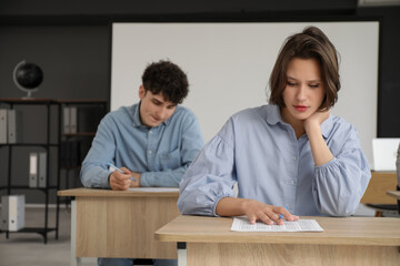 Female student passing exam at desk in classroom