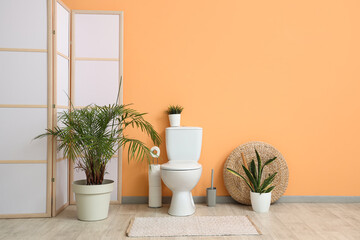 Interior of restroom with toilet bowl and plants near beige wall