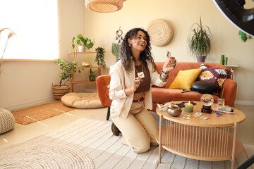 Young African-American witch with runes recording video at home