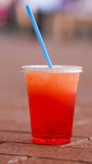 Refreshing Mixed Fruit Drink with Ice and Blue Straw in Clear Plastic Cup – Summer Beverage with Red and Yellow Layers