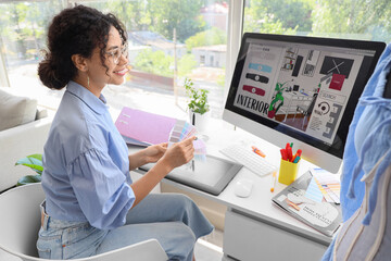 Female African-American graphic designer with color palettes working at table in office