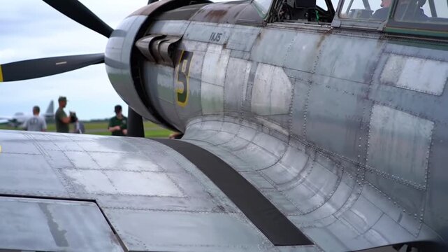 Close-up of a vintage warbird aircraft with riveted metal panels and propeller detail on an airfield