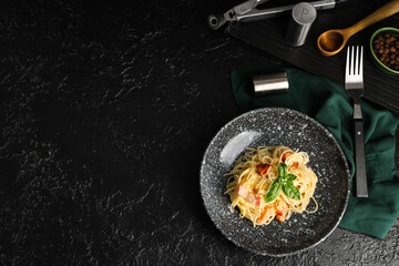 Bowl with tasty pasta carbonara, fork and napkin on dark background