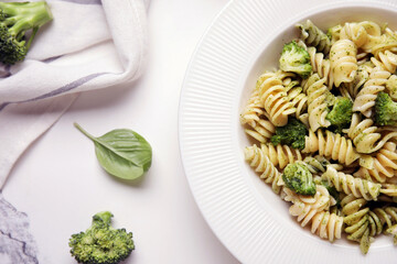 Plate of delicious fusilli pasta with broccoli and basil leaf on white background