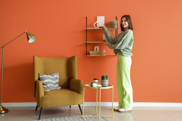 Obraz premium Young woman pointing at frame on shelf near armchair at home