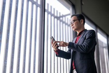 Businessman using smartphone near office window with vertical blinds