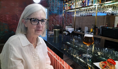 Elderly Woman Enjoying a Drink at a Bar Counter with Snack