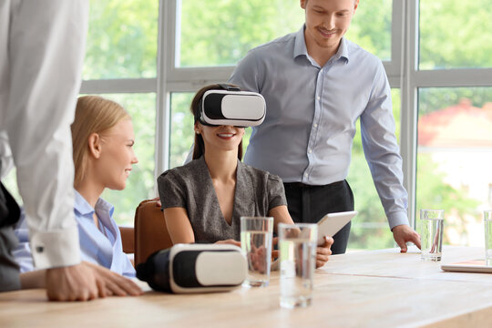 Young businesswoman using VR glasses with her colleagues at table in office