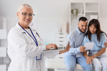 Fototapeta premium Female fertility doctor using laptop against couple after IVF in clinic