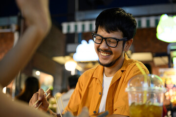 Happy man eating with chopsticks at night market and smiling