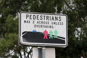 Fototapeta premium Road sign telling pedestrians to walk no more than two side by side unless someone is overtaking with a tree in the background