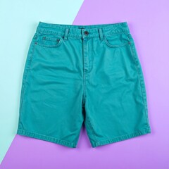 Turquoise denim shorts laid flat on a pastel background.