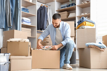 Young man packing clothes into wardrobe box in dressing room