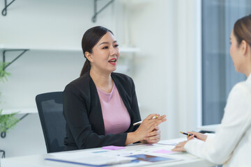 Two asian businesswomen are discussing during a meeting in the office, reviewing documents and graphs, collaborating on a project
