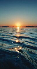 Calm ocean sunset.  Distant hazy mountains.  Golden sun.  Reflective water surface
