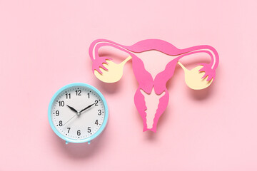 Clock with paper uterus on pink background. Gynecology concept