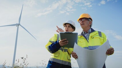 Two Caucasian coworkers standing in middle of large field. Man with glasses holding large building plan. Woman with notepad providing information. Pointing at information on paper. Man listening.