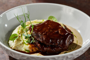 Braised beef cheek with mashed potatoes and demi-glace, moody lighting, closeup composition