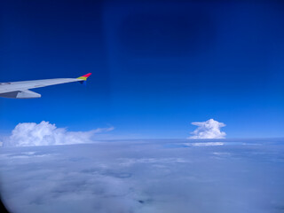 Airplane wing view above the clouds, showing bright blue sky, fluffy white formations, and stunning aerial scenery that captures the beauty of flight and peaceful travel moments.