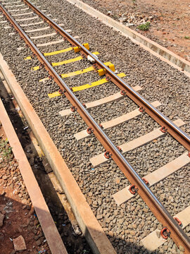 Railway track detail with metal rails, sleepers, and gravel bed, featuring yellow safety markings, capturing infrastructure design and maintenance elements in a transport system