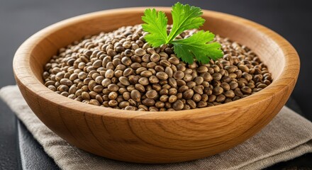 Obraz premium A wooden bowl filled with hemp seeds, topped with fresh green herb leaves, sits on a dark surface.