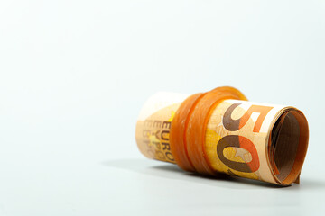 Rolled 50 euro banknotes secured by an orange rubber band lying on a white background represent savings, investment, and financial security