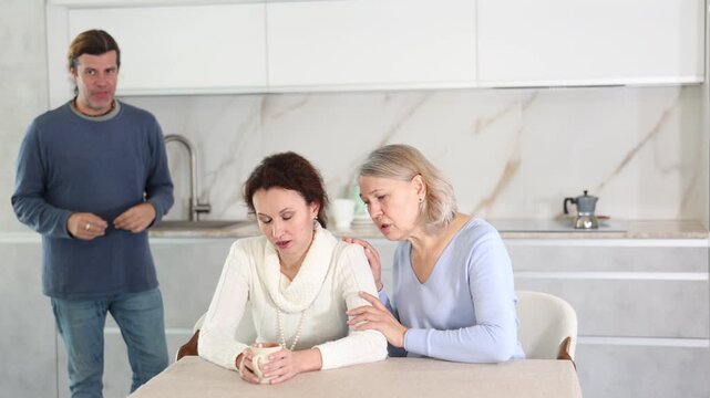 Woman sits near daughter and comforts during quarrel with husband. Mother calms upset daughter takes side of woman in altercation with adult brother. Man is outraged by girlfriend behavior and blames