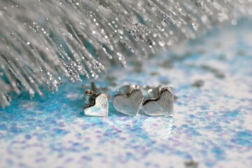 Elegant silver heart-shaped earrings on a glitter blue background, ideal for any occasion.