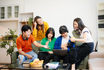 Group of young Asian students working on a project with laptops and tablets. Cozy indoor setting, teamwork,