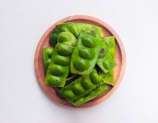 Raw Petai (Parkia Speciosa) or Bitter Bean in a wooden plate on a white background.